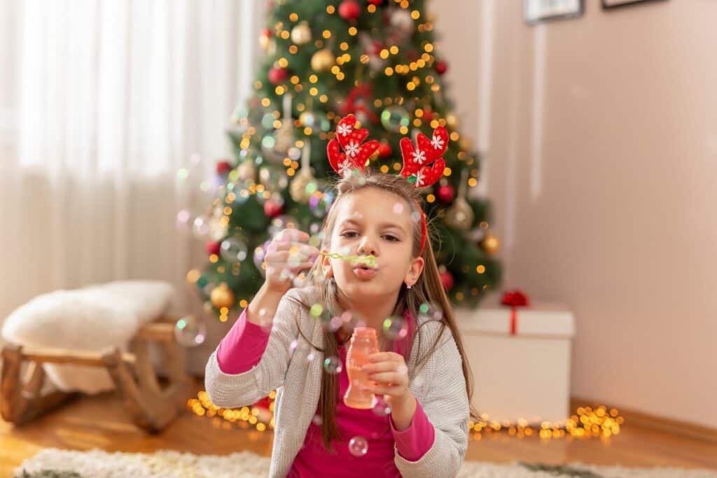 fillette qui fait des bulles devant un sapin de Noël