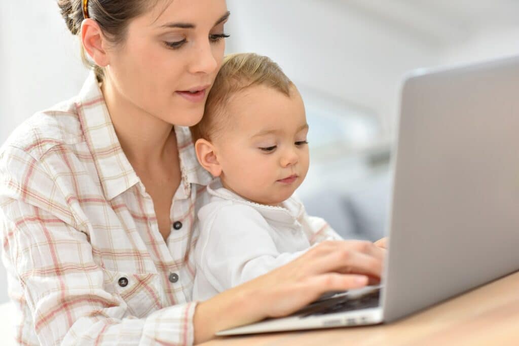 maman sur ordinateur avec bébé dans les bras