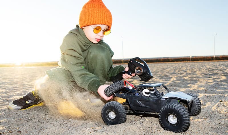 garçon sur la plage avec une voiture télécommandée tout terrain