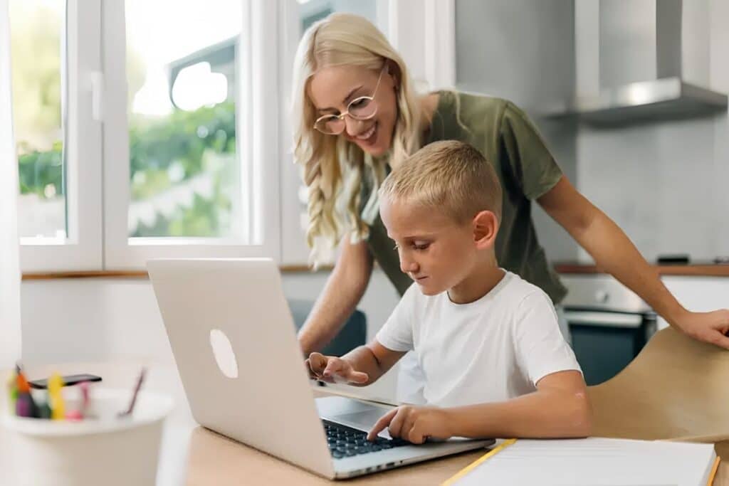 enfant sur un ordinateur portable avec sa maman derrière