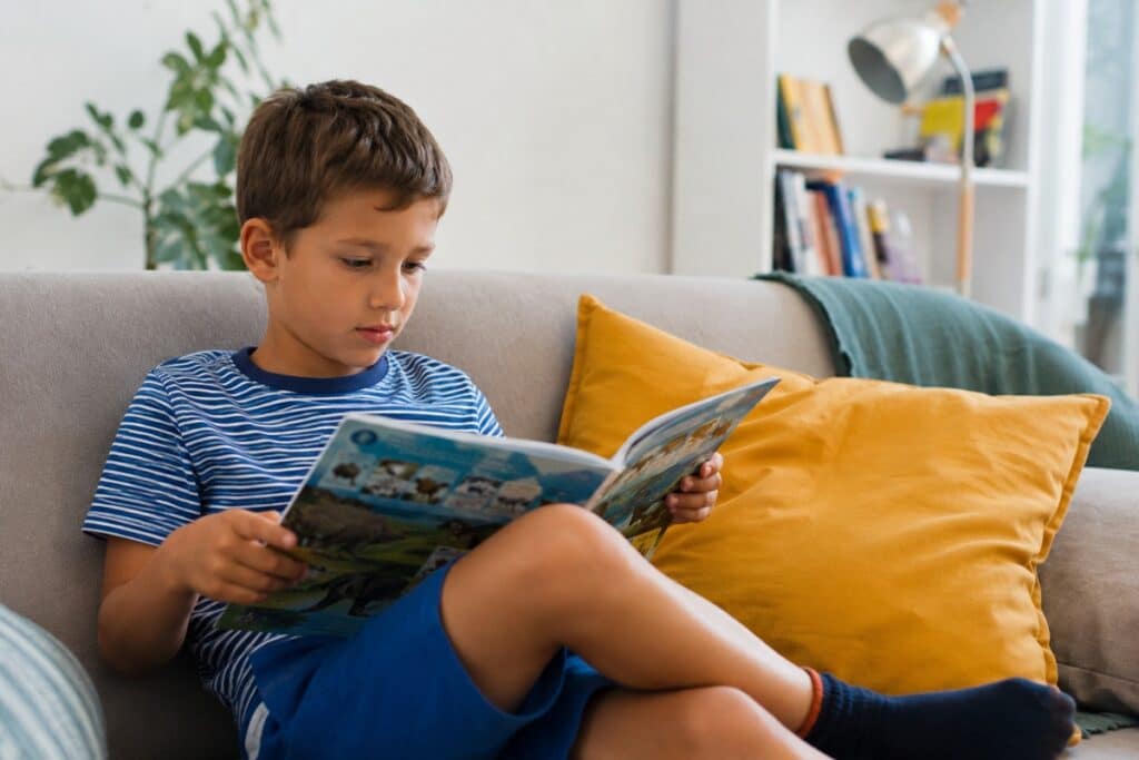 garçon assis dans un canapé avec un magazine dans les mains