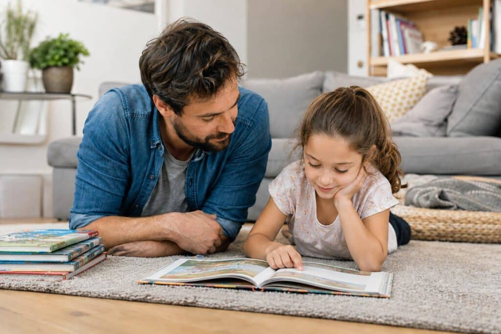 jeune fille lisant un livre allongé sur un tapis avec son papa